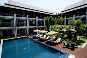 a swimming pool with chairs and umbrellas next to a building at De Lanna Hotel in Chiang Mai