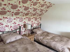 two beds in a room with floral wallpaper at George's House - 1 Leacklee in Manish