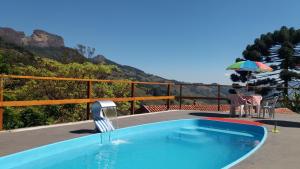 a swimming pool with an umbrella next to a mountain at chales azaleia todos in São Bento do Sapucaí