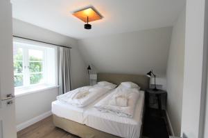 a bedroom with a bed with white sheets and a window at Ulenhüs in Wenningstedt