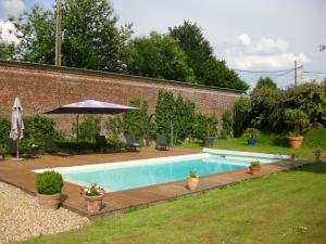 a swimming pool with a wooden deck and an umbrella at Château de Cleuville in Cleuville