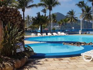 a large swimming pool with chairs and palm trees at Apartamento Beira Mar in Caraguatatuba