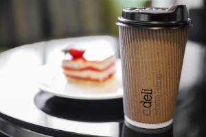 a coffee cup sitting on a table with a plate of cake at Centro Salama Jeddah by Rotana in Jeddah