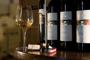 una copa de vino blanco junto a tres botellas de vino en Alloggio Agrituristico CORTE SAN BIAGIO, en Corno di Rosazzo