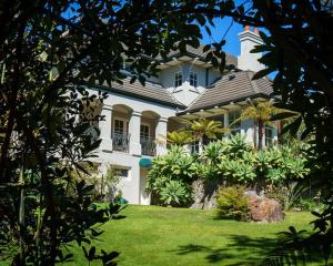 a large white house with a garden in front of it at Greenmantle Estate Hotel in Paraparaumu