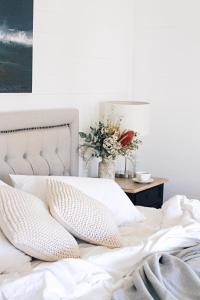 a white bed with pillows and a table with a vase of flowers at Bangalow Guesthouse in Bangalow