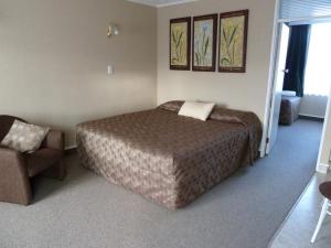 a bedroom with a bed and a chair at Monarch Motel in Invercargill