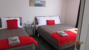 a bedroom with two beds with red pillows and a mirror at Ahuriri Motels in Omarama