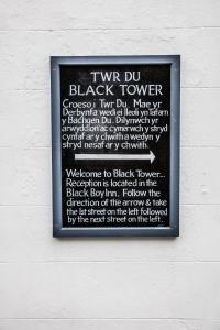 una señal en el costado de una pared con una torre negra en The Black Boy Inn, en Caernarfon