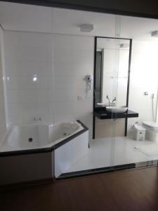 Baño blanco con bañera y lavamanos en Rota Hoteis Itumbiara, en Itumbiara