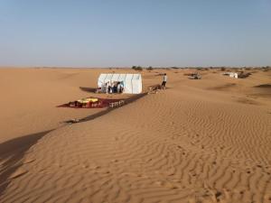 un grupo de personas de pie alrededor de una tienda en el desierto en Erg Lihoudi Dunes & Bivouac, en Mhamid