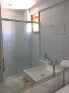 un bagno piastrellato bianco con lavandino e specchio di Apartamento 01 Enseada Praia do Forte a Praia do Forte