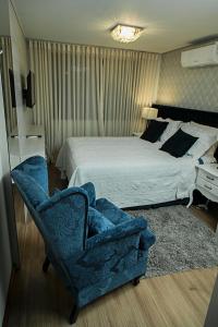a bedroom with a bed and a blue chair at Ednamar Apartmentos Gramado Siena in Gramado