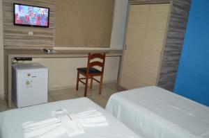 a hotel room with two beds and a chair and a television at Pousada Ayrumã in Itapipoca