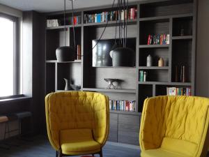 2 sillas amarillas en una sala de estar con estanterías en Campanile Muenchen Sendling, en Múnich