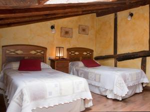 a bedroom with two beds with white sheets and red pillows at Casa Rural El Encuentro in Villalón de Campos