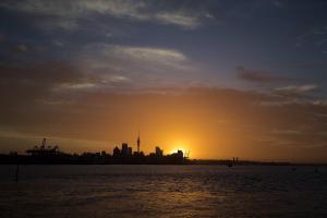 a city skyline with the sun setting in the background at Auckland Waterfront Serviced Apartments on Prince's Wharf in Auckland