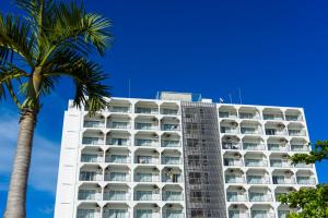 a tall white building with palm trees in front of it at Condominium Hotel Monpa in Chatan +25 photos