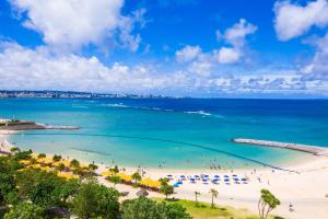 a beach with people and umbrellas and the ocean at Condominium Hotel Monpa in Chatan