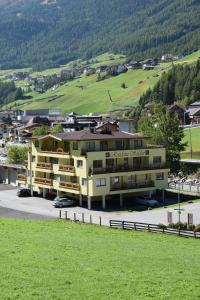 ein großes gelbes Gebäude auf einem Parkplatz mit grünem Feld in der Unterkunft A Casa Residenz in Sölden