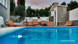 a swimming pool with chairs and a table at Salis Apartments in Vrsi