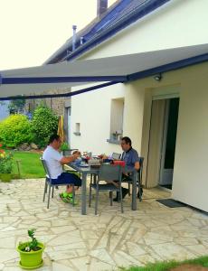 twee mannen aan een tafel onder een paraplu bij Chambres d'hôtes La Pinderie in Bazouges-la-Pérouse