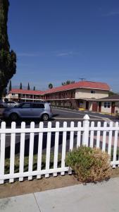 a white picket fence with a car in a parking lot at Valley Hotel in Rosemead