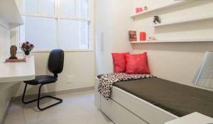 Habitación pequeña con cama con almohadas rojas y silla en Suítes e Quartos na Avenida Carlos Gomes, en Porto Alegre