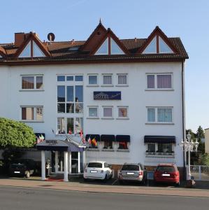 un grand bâtiment blanc avec des voitures garées devant lui dans l'établissement Hotel Irmchen, à Maintal