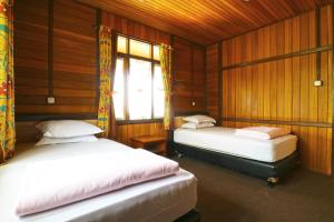 two beds in a room with wooden walls and a window at Villa Gardenia Bandung in Lembang