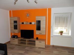 a living room with an orange wall and a tv at Ferienwohnung Gänseblümchen in Wartenburg