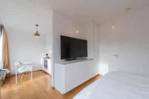 een witte slaapkamer met een flatscreen-tv aan de muur bij Studio des jardins suspendus in Luik