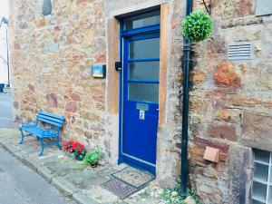 una puerta azul y un banco junto a un edificio de ladrillo en The Gables, en Crail