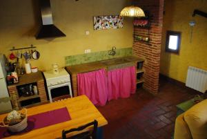 a kitchen with a table and a stove with pink curtains at Masia El Canalot - Molí Del Pont in Cornudella