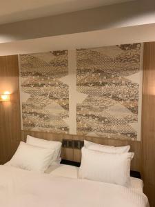 ein Bett mit weißen Kissen und ein Gemälde an der Wand in der Unterkunft Hotel Be-zen shimanouchi in Osaka