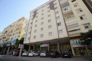 un grand bâtiment blanc avec des voitures garées devant lui dans l'établissement Bulvar Hotel, à Antalya