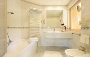 ein weißes Badezimmer mit einer Badewanne und einem Waschbecken in der Unterkunft Hotel Garni Concordia - Dolomites Home in Wolkenstein in Gröden