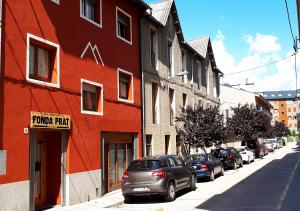 un bâtiment rouge avec des voitures garées sur le côté d'une rue dans l'établissement Hostal Fonda Prat, à Puigcerdà