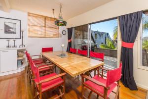 uma sala de jantar com uma mesa de madeira e cadeiras vermelhas em Bayswater Holiday Home em Paihia