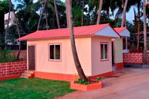una pequeña casa con techo rojo junto a una palmera en Sushegad Holiday Homes, en Ratnagiri