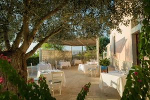 a patio with white tables and chairs under a tree at Masseria Bandino & Spa in Otranto