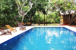 a blue swimming pool with two chairs and trees at Bissa Villa in Habarana