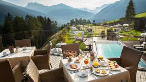 - une table avec des assiettes de nourriture sur un balcon avec une piscine dans l'établissement Hotel Albion Mountain Spa Resort Dolomites, à Ortisei