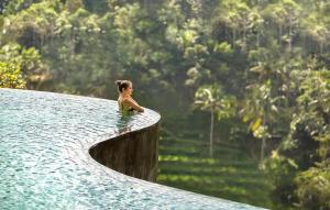 a woman sitting on the edge of a pool of water at The Kayon Jungle Resort in Ubud