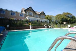 a swimming pool with white chairs in front of a house at Luccombe Manor Country House Hotel in Shanklin