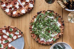 three pizzas sitting on a wooden table at Boro Hotel in Queens
