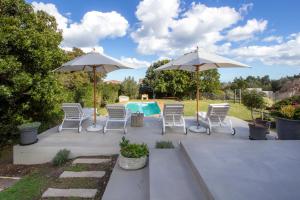 a patio with chairs and umbrellas and a pool at Protea & Pincushion Cottages in Hermanus