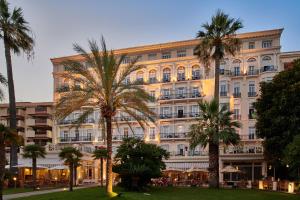 un grand bâtiment avec des palmiers devant lui dans l'établissement Hôtel Vacances Bleues Royal Westminster, à Menton