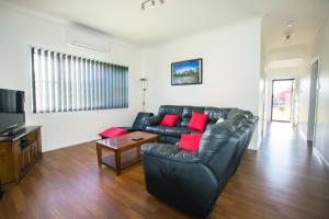 a living room with a black leather couch and red pillows at Topaz Cottage in Glen Innes