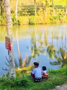 a man and a child sitting next to a lake at Alam Taman Villa in Tabanan